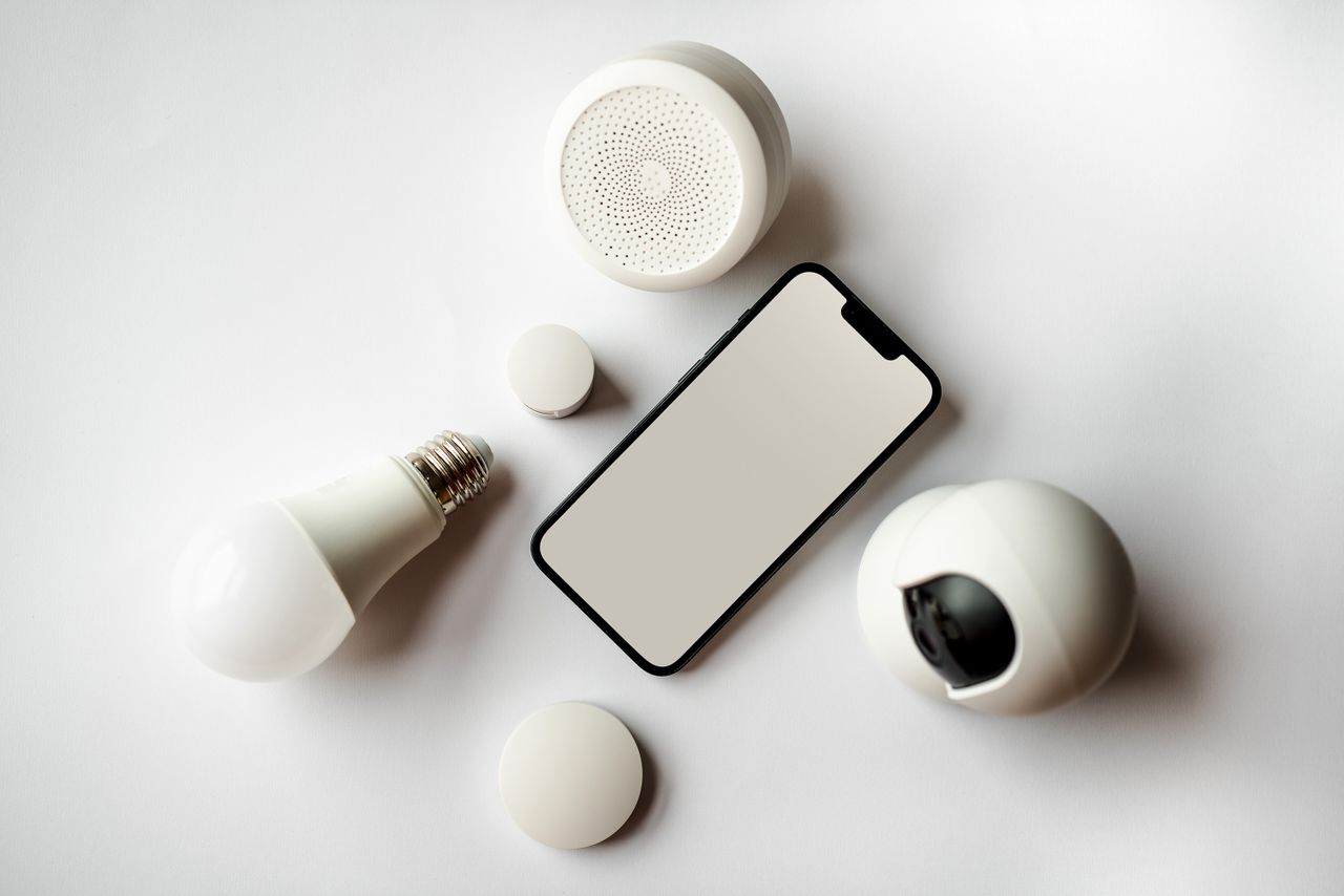 services-01 Flat lay of smartphone and smart home devices on a white backdrop, showcasing modern technology.