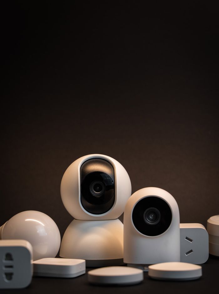 hero-img-01 Close-up of modern white security cameras and smart home devices with dark background.